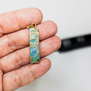 May include: Gold pendant with a rectangular turquoise and gold stone. The stone has a marbled pattern of blue, green, and gold.