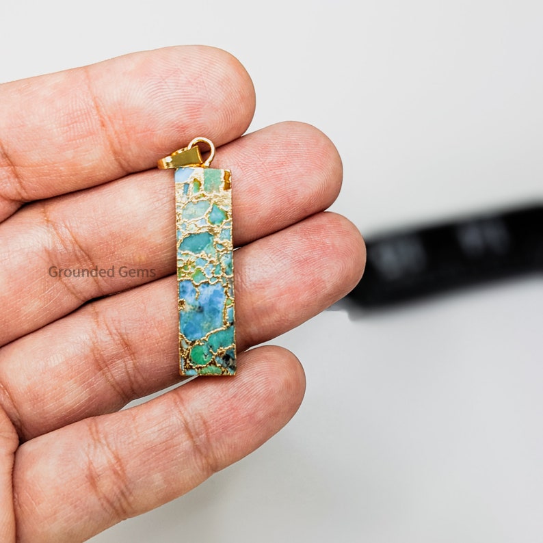 May include: Gold pendant with a rectangular turquoise and gold stone. The stone has a marbled pattern of blue, green, and gold.