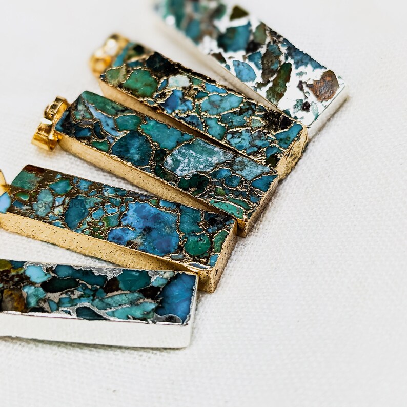 May include: Five rectangular turquoise and gold pendants with a marbled pattern. The pendants are arranged in a fan shape on a white surface.