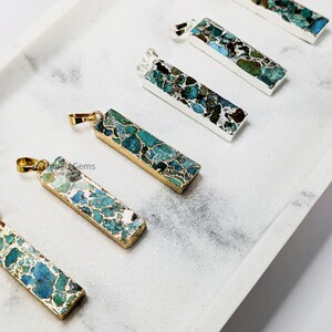 May include: Five gold and silver pendant charms with a turquoise and green marbled stone design. The pendants are rectangular in shape and have a gold or silver bail.
