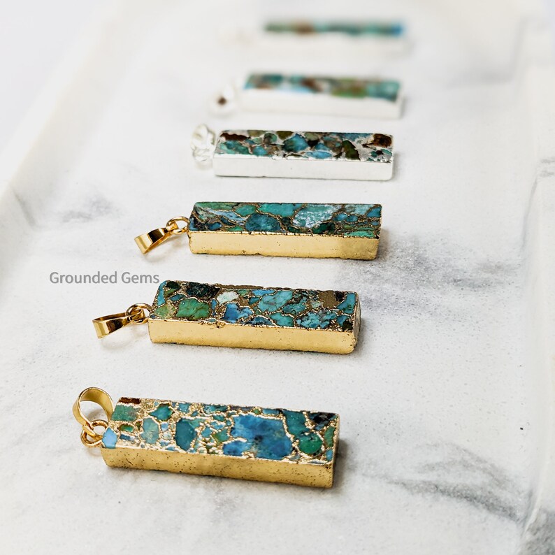 May include: A set of six gold-plated bar pendants with a blue and green marbled pattern. The pendants are arranged in a row on a white surface. The text "Grounded Gems" is visible in the lower left corner of the image.