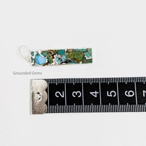 May include: A silver pendant with a rectangular turquoise stone. The stone has a mottled pattern of blue, green, and brown. The pendant is approximately 1.5 inches long.