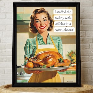 Puede incluir: Impresión enmarcada de estilo vintage que muestra a una mujer sosteniendo un pavo asado en una fuente. Lleva un delantal amarillo y una camisa a rayas verdes. El texto dice: "¡Rellené el pavo con comestibles este año...salud!" La impresión está en un marco negro.