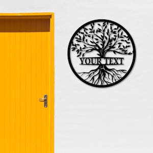 K&ouml;nnte beinhalten: Schwarze Metall-Wandkunst mit einem Lebensbaum. Das Design zeigt einen Baum mit Wurzeln, &Auml;sten und Bl&auml;ttern, der von einem kreisf&ouml;rmigen Rahmen umschlossen ist. Der Text "YOUR TEXT" wird &uuml;ber der Mitte des Baumes angezeigt. Hintergrund ist eine wei&szlig;e Wand mit gelber T&uuml;r.