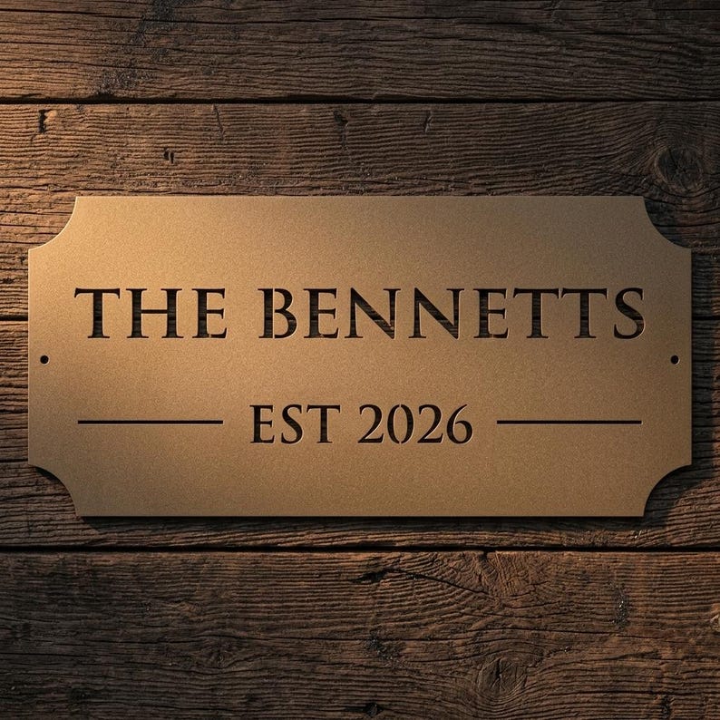 Pode incluir: Uma placa retangular de metal na cor bronze com cantos arredondados e dois pequenos orif&iacute;cios de montagem nas laterais. A placa apresenta o texto cortado a laser THE BENNETTS em fonte serifada, com o texto EST 2026 centralizado abaixo entre duas linhas.