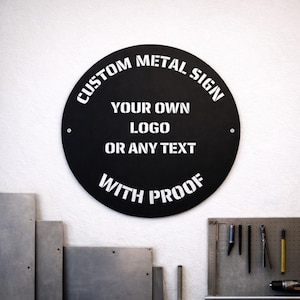 Puede incluir: Un letrero metálico circular negro con texto blanco que dice "CUSTOM METAL SIGN, YOUR OWN LOGO OR ANY TEXT, WITH PROOF". El letrero está montado en una pared blanca. Es probable que el letrero sea personalizado.