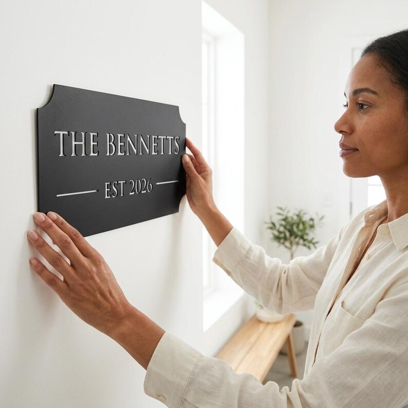 Pode incluir: Uma placa de parede retangular de metal preto com bordas curvas decorativas. A placa apresenta o texto cortado a laser THE BENNETTS em uma fonte serifada, seguido pelo texto EST 2026 centralizado entre duas linhas horizontais.