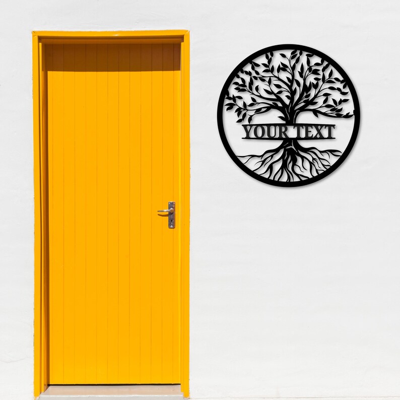 K&ouml;nnte beinhalten: Schwarze Metall-Wandkunst mit einem Lebensbaum. Das Design zeigt einen Baum mit Wurzeln, &Auml;sten und Bl&auml;ttern, der von einem kreisf&ouml;rmigen Rahmen umschlossen ist. Der Text "YOUR TEXT" wird &uuml;ber der Mitte des Baumes angezeigt. Hintergrund ist eine wei&szlig;e Wand mit gelber T&uuml;r.