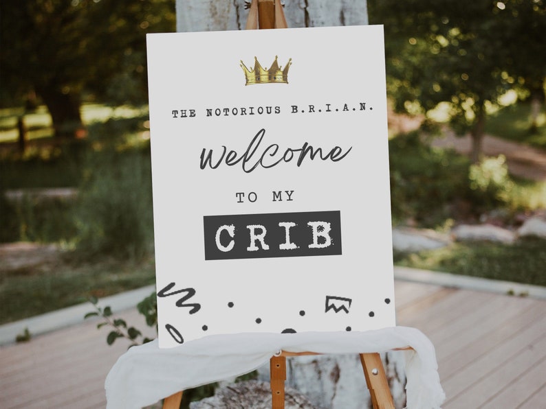 K&ouml;nnte beinhalten: Ein wei&szlig;es Schild mit schwarzem Text, der "The Notorious B.R.I.A.N. welcome to my CRIB" lautet, mit einer goldenen Krone &uuml;ber dem Text. Das Schild steht auf einem Staffelei und hat schwarze Kritzel-Akzente am unteren Rand.
