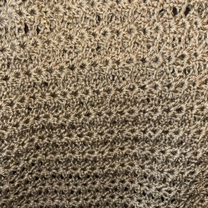 May include: Close-up of a crocheted fabric with a textured, starburst pattern. The yarn is a neutral, light brown color, creating a warm and inviting aesthetic. The detailed stitching is visible throughout the image.
