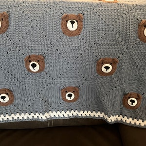 Pode incluir: Um cobertor de bebé azul em crochê com uma borda branca e aplicações de urso castanho.