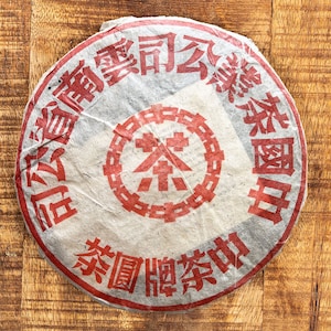 Peut inclure: Un gâteau de thé rond et blanc avec des caractères chinois rouges. Les caractères se lisent "云南 滇红 茶饼" (Yunnan Dianhong Tea Cake).