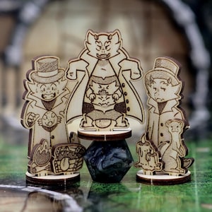 May include: Wooden figurines of cartoon cats in coats and top hats. The central figure stands on a dark blue stone, flanked by two others. Accessories include a treasure chest, a candle, and a small animal.