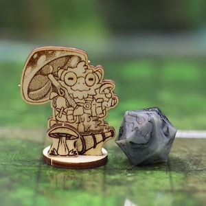 May include: A wooden miniature figurine of a mushroom person holding a mushroom, standing on a mushroom base. The figurine is next to a grey and white dice.