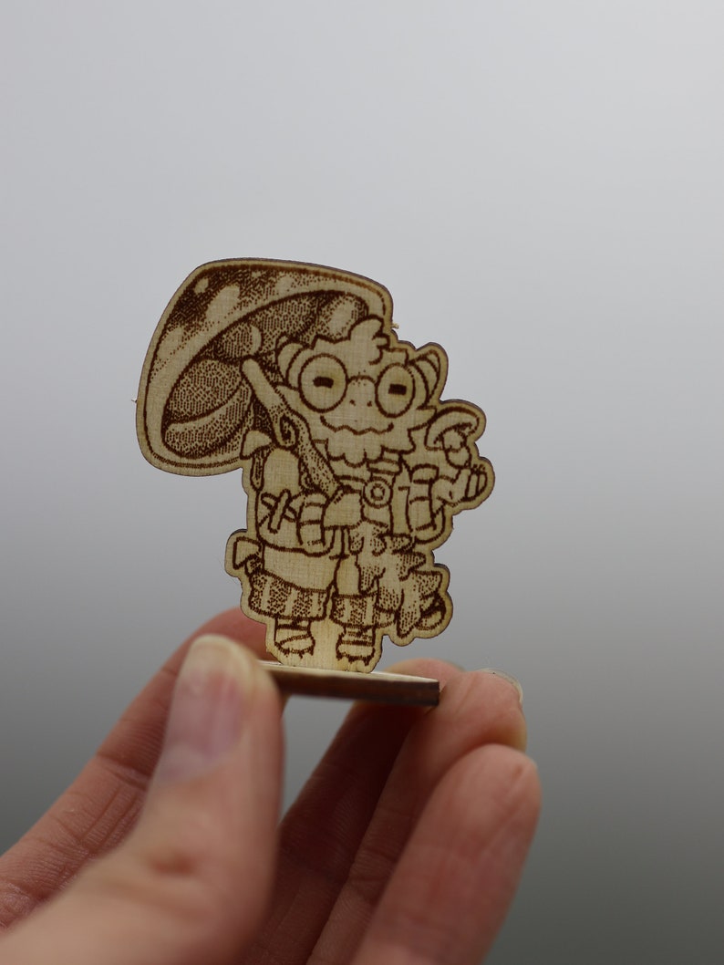 May include: A wooden figurine of a cartoon character with a mushroom cap, wearing a backpack and holding a stick. The character has large eyes and a friendly expression.