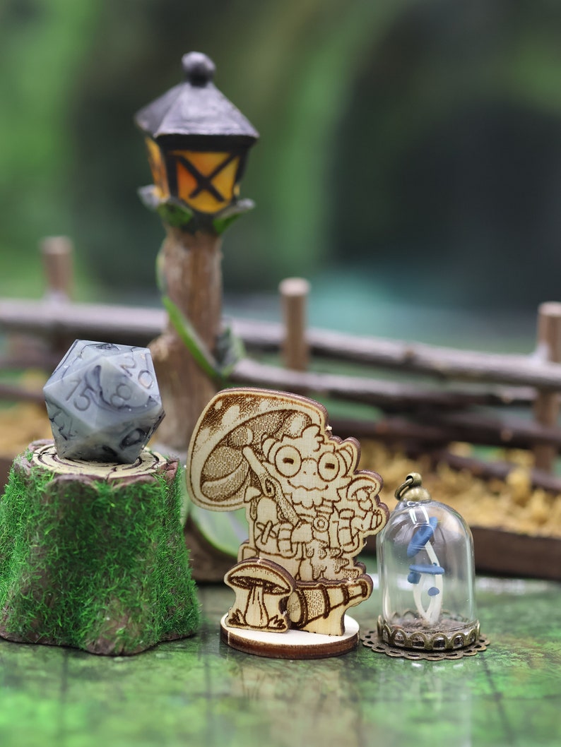 May include: A wooden miniature figurine of a character holding a mushroom and a lantern, standing on a wooden base. A grey and white dice is on a wooden stump with green moss. A glass dome with a blue and white flower inside sits on a wooden base.