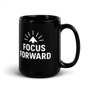 Pode incluir: Caneca de cerâmica preta com a inscrição branca "FOCUS FORWARD" e um desenho de seta e linhas. A caneca tem uma pega grande e um acabamento brilhante. Adequada para café ou chá.