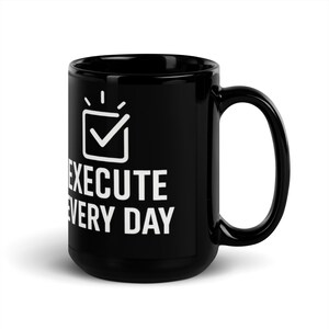Op de afbeelding: Zwarte keramische koffiemok met een wit vinkje-icoon en de tekst "EXECUTE EVERY DAY".