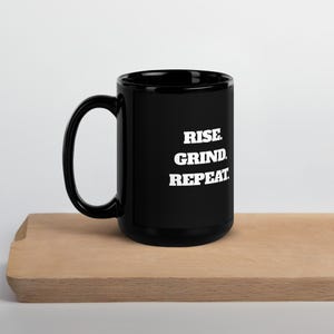 May include: Black ceramic mug with a white inscription that reads "Rise. Grind. Repeat."