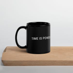 Può includere: Una tazza da caffè in ceramica nera con una scritta bianca che recita "TIME IS POWER".