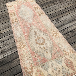 May include: A vintage Turkish runner rug in a faded pink and cream colour scheme. The rug features a traditional geometric pattern with a central medallion.