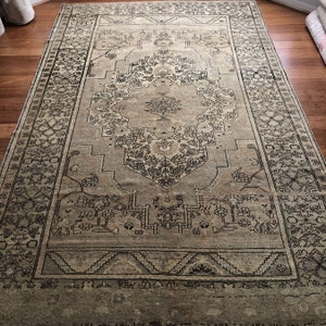 May include: A vintage rug with a beige background and a black geometric pattern. The rug has a central medallion with a floral design and a border with a repeating pattern.