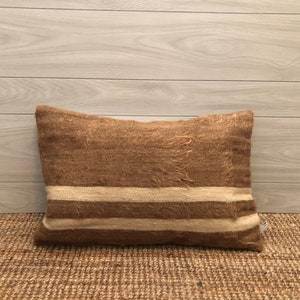 May include: A brown and white striped throw pillow with a fuzzy texture. The pillow is sitting on a brown woven rug.