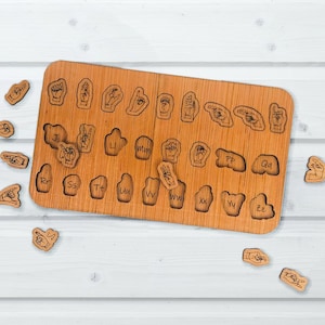 May include: A wooden board with cutouts for each letter of the alphabet in American Sign Language.  The board is surrounded by individual wooden tiles with the sign language alphabet on them.