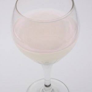 May include: A clear glass wine glass filled with a light pink liquid.