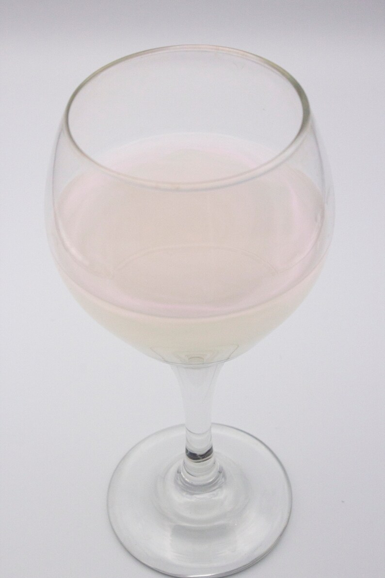 May include: A clear glass wine glass filled with a light pink liquid.