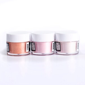 May include: Three small jars of metallic luster dust in shades of peach, pink, and white. The jars have white lids and black labels with a QR code.