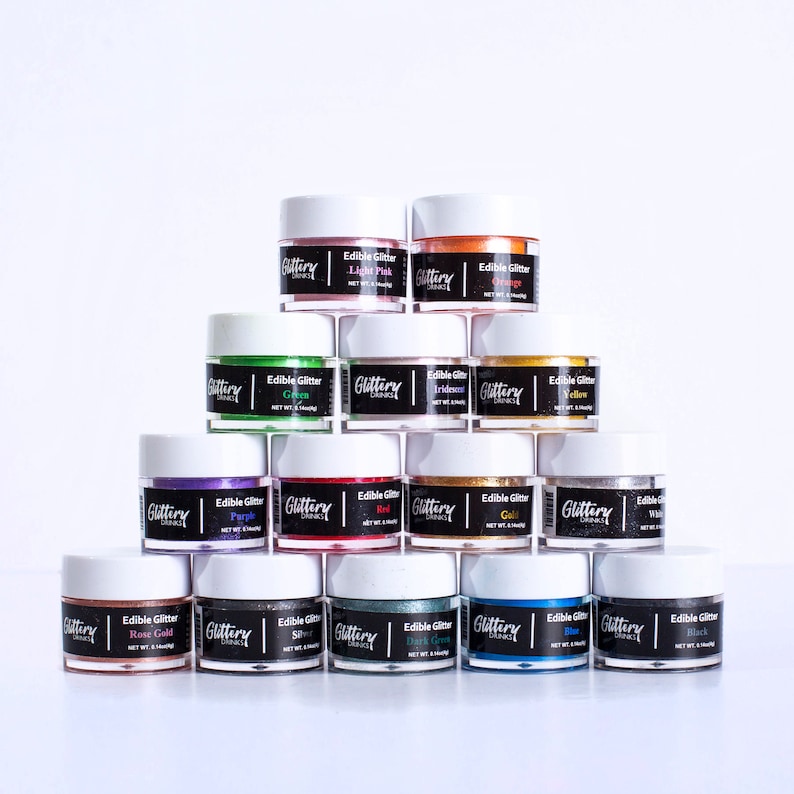 May include: A collection of 12 small jars of edible glitter in various colors, including light pink, green, iridescent, yellow, purple, red, gold, white, rose gold, silver, dark green, blue, and black. Each jar has a white lid and a black label with the text "Glittery" and the color of the glitter.