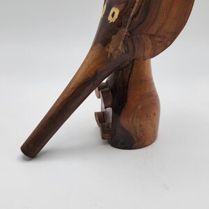 May include: A wooden elephant figurine with a long trunk and large ears. The elephant is carved from dark brown wood and has two small yellow circles for eyes.