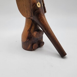 May include: A wooden elephant figurine with a long trunk and large ears. The elephant is painted with brown and black stripes and has yellow eyes.