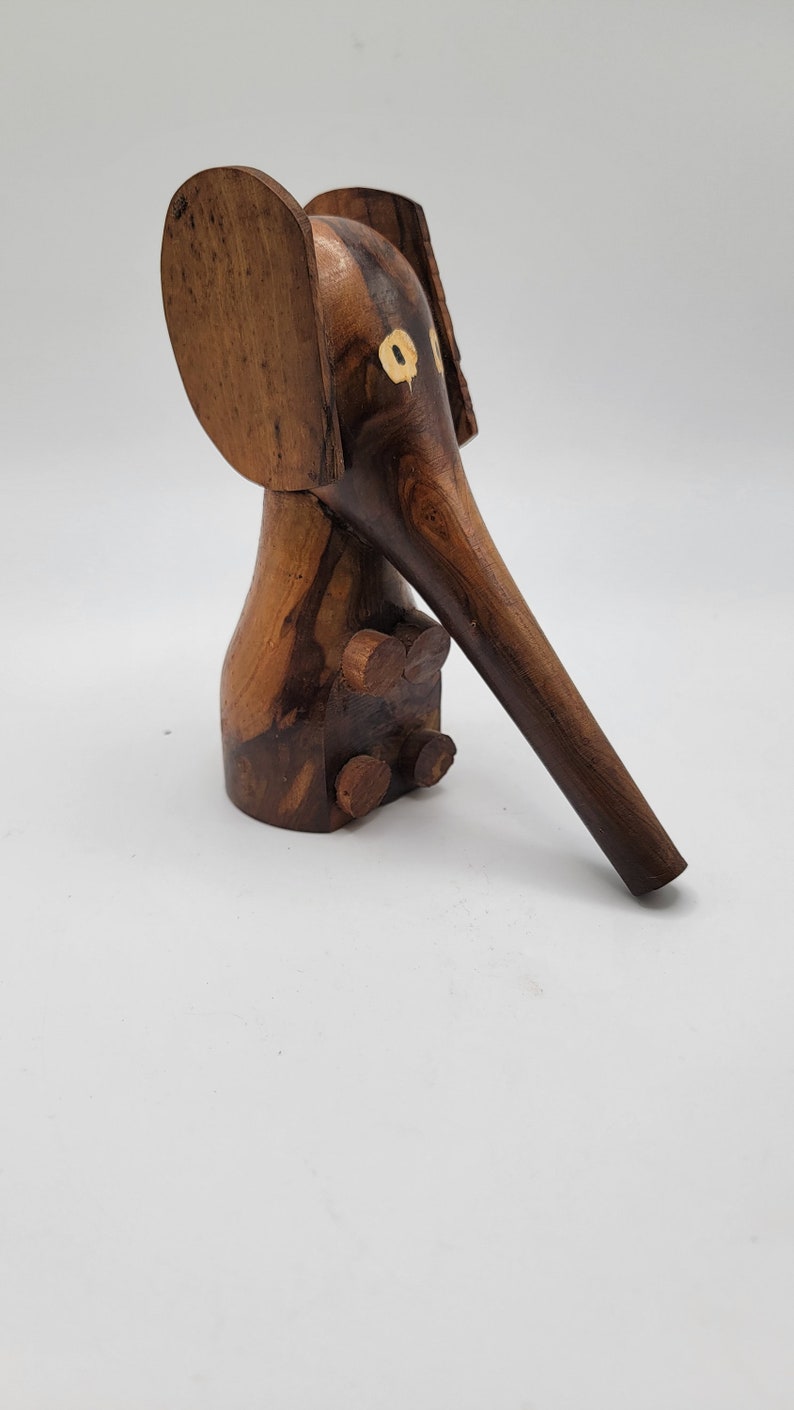 May include: A wooden elephant figurine with a long trunk and large ears. The elephant is painted with brown and black stripes and has yellow eyes.