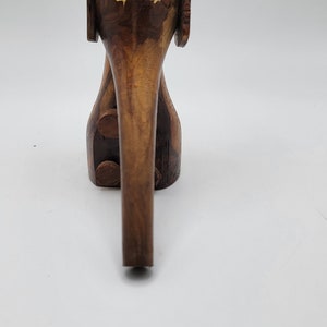 May include: A wooden elephant figurine with a brown and dark brown wood grain pattern. The elephant has large ears and a long trunk. The eyes are inlaid with yellow wood.