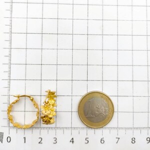 May include: Two gold-colored hoop earrings with a floral design. The earrings are next to a one Euro coin. The earrings are approximately 1 inch in diameter.
