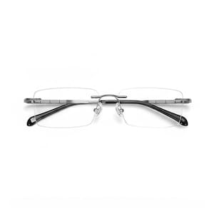 May include: Rimless eyeglasses with rectangular lenses. The frame is silver-toned with black temples. The nose pads are clear. The glasses are designed for vision correction and are suitable for everyday use.