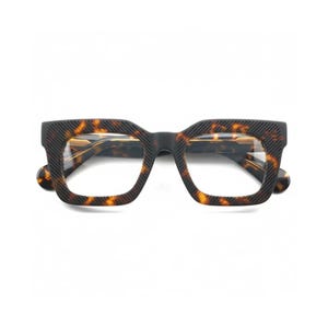 Può includere: Occhiali dalla montatura quadrata con motivo tartarugato. Le montature presentano un design strutturato e scanalato in marrone scuro e nero. Le lenti sono trasparenti e lo stile generale è moderno e audace.