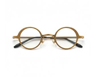 May include: Gold-toned, round eyeglasses with a classic design. The frames feature a textured pattern around the lenses and sleek black temples. The glasses have a minimalist aesthetic, suitable for everyday wear.