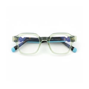 Könnte beinhalten: Eine Brille mit hellgrünem Rahmen und quadratischen Gläsern. Die Bügel haben einen blauen Akzent und der Innenrahmen hat ein Schildpattmuster. Die Brille ist vor einem weißen Hintergrund platziert.