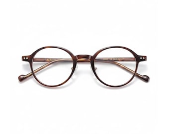 Może przedstawiać: Okrągłe okulary z brązową oprawką w kolorze żółwia i złotymi zausznikami. Okulary mają klasyczny, vintage design. Soczewki są przezroczyste. Oprawka wykonana jest z wytrzymałego materiału. Okulary nadają się do codziennego użytku.