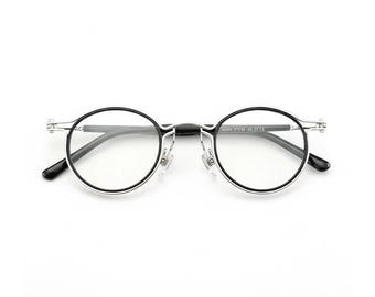 May include: Round eyeglasses with black rims and silver bridge. The glasses have clear lenses and black temples. The text "ACUUS 47[]21-135 CE" is printed on the temple. The glasses are set against a white background.