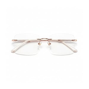 May include: Rimless eyeglasses with a rose gold frame and clear lenses. The temples are embellished with small, sparkling crystals. The glasses have a minimalist design, suitable for everyday wear. The overall aesthetic is modern and elegant.