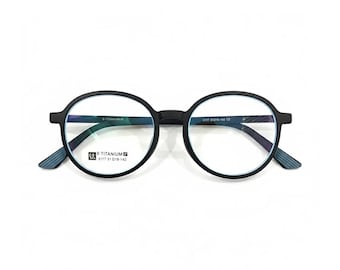 May include: Black round-frame eyeglasses with blue-gray temple tips. The glasses have a matte finish and feature the text "B-TITANIUM" and "5117 51 018-142" on the frame. The lenses are clear.