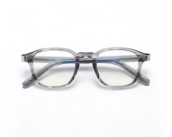 Könnte beinhalten: Eine Brille mit grauem, quadratischem Rahmen und klaren Gläsern. Die Brille hat ein subtiles, durchscheinendes Aussehen und ist vor einem weißen Hintergrund platziert. Die Rahmen sind in einem neutralen Grauton gehalten.