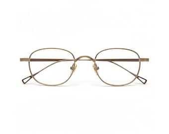 May include: A pair of gold-colored eyeglasses with a thin metal frame. The lenses are clear, and the frames have a rounded shape. The temples have a geometric design at the ends. The glasses are set against a white background.