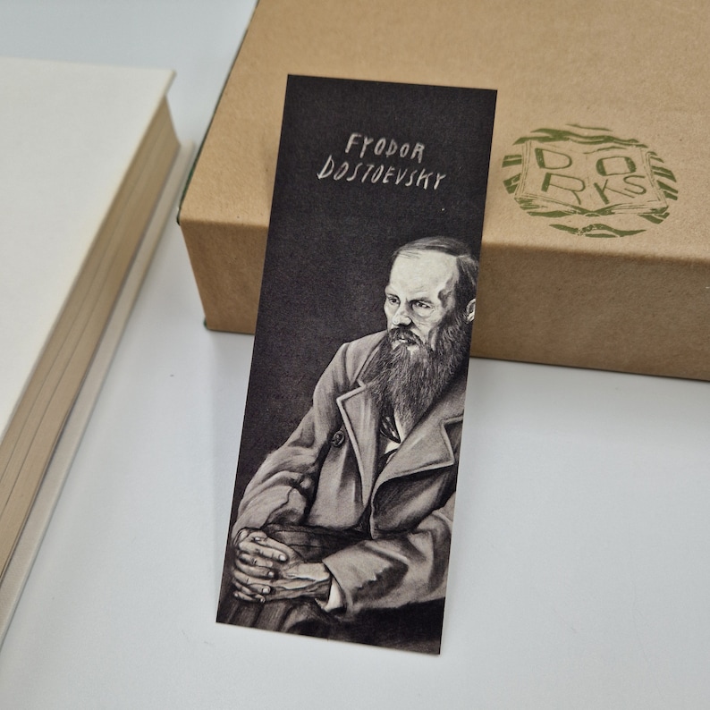 May include: A black and white bookmark featuring a portrait of Fyodor Dostoevsky, a Russian novelist. The bookmark has the text "Fyodor Dostoevsky" written in white on a black background.