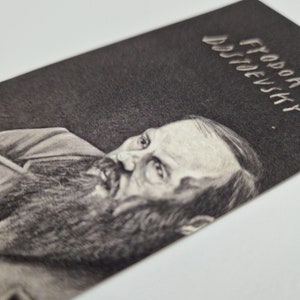 May include: A black and white pencil drawing of Fyodor Dostoevsky, a famous Russian author. The drawing is on a dark background with the name "Fyodor Dostoevsky" written in white lettering at the top.