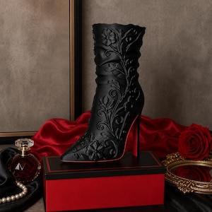 May include: A black ankle boot with a pointed toe and a high stiletto heel, featuring an intricate embossed floral and vine pattern across the entire surface. The interior of the heel and the sole edge are finished in a vibrant red color.